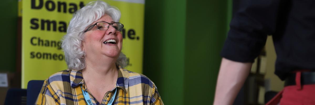 A smiling woman sitting behind a reception desk looks up at a visitor.