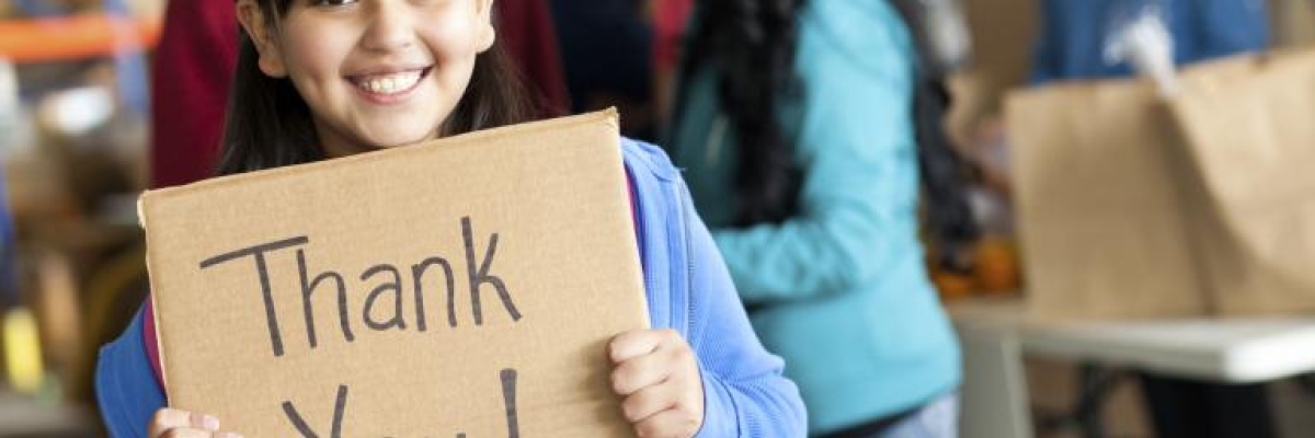 A young girl smiles and holds a cardboard sign that reads 'thank you!' 
