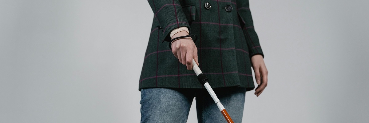 A person with a white cane poses for a photo in an office corridor. 