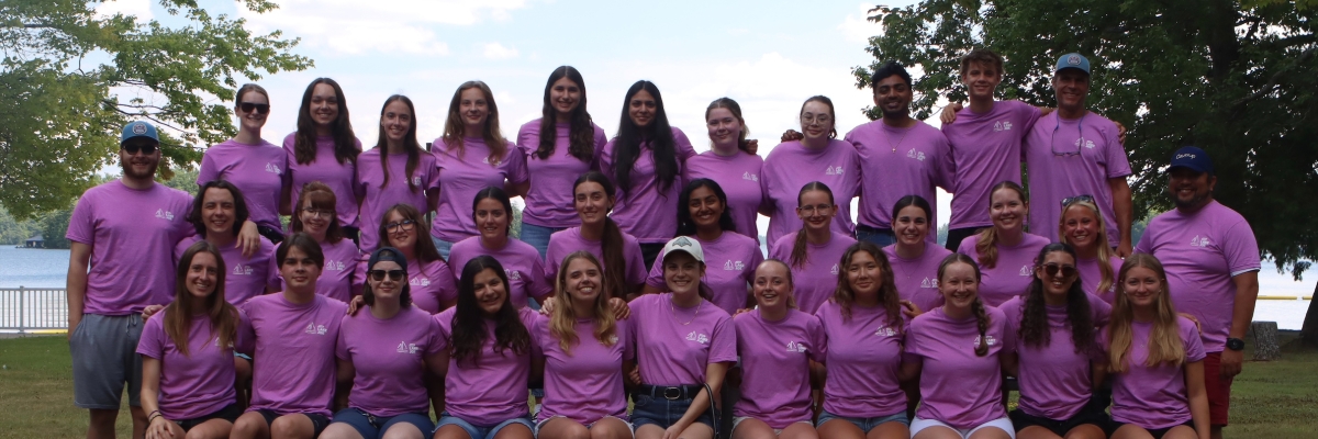 The 2026 seasonal staff team is posing on the lawn. There are 34 people wearing shorts and pink tshirts.