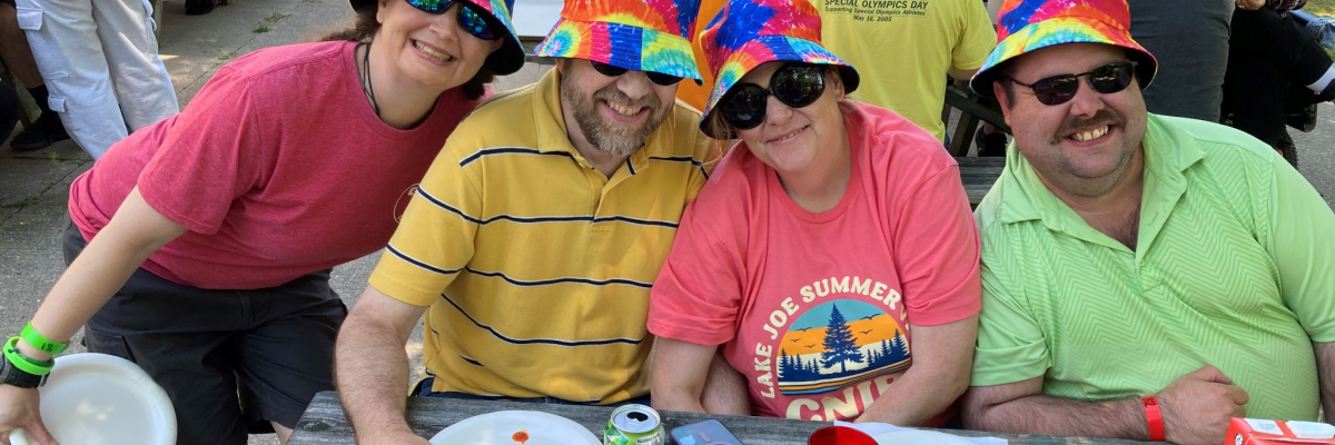 Four people eat lunch outdoors wearing bright t-shirts and bucket hats 