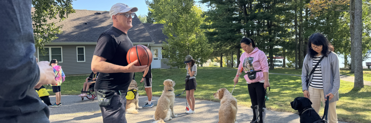 An instructor stands outside in front of a line of participants and guide dogs.