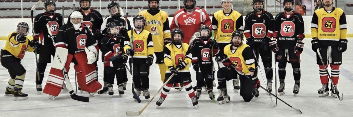 The Ottawa Blind Hockey children and youth team pose for a group photo on the rink. They are all wearing hockey equipment and holding hockey sticks.