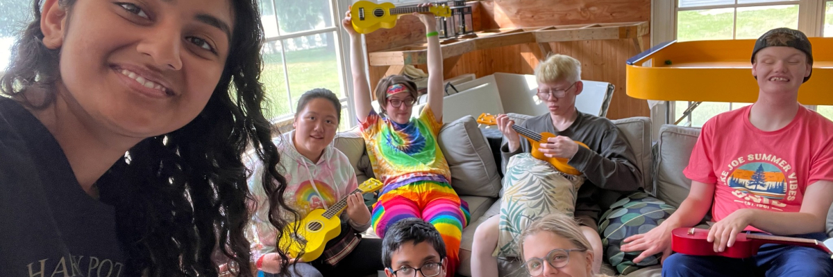 A female counsellor is standing in front of a group of participants playing ukeleles.