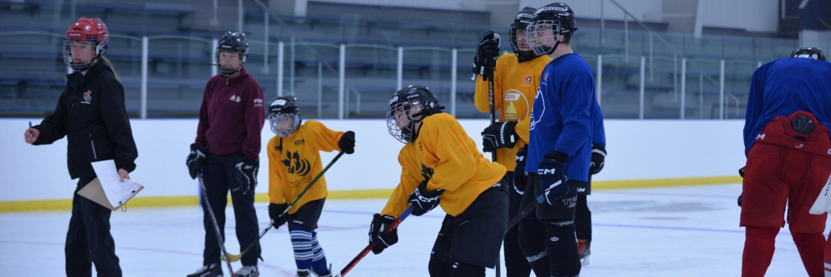 Coach guiding young players on the ice. Players are wearing yellow and blue jerseys