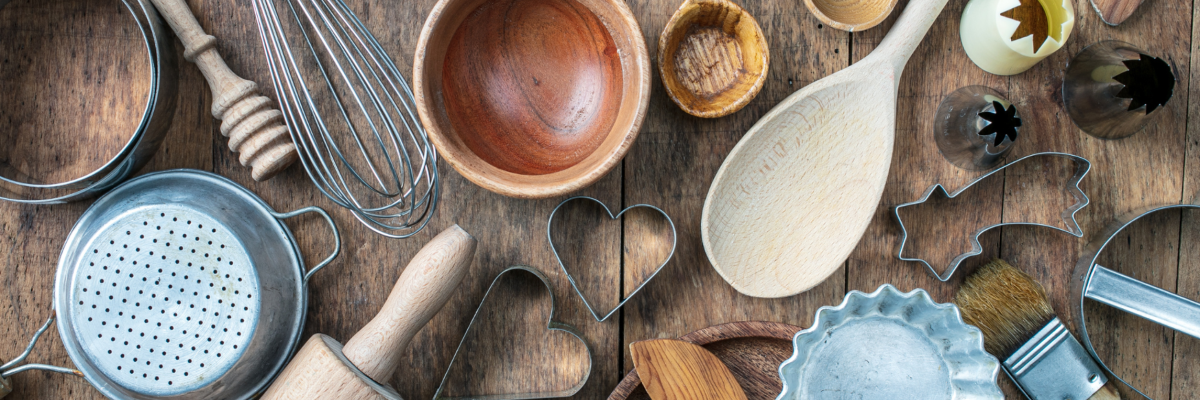 Bird's eye view of a variety of baking tools on a wooden table: spoons,, rolling pins, cookie cutters, etc.