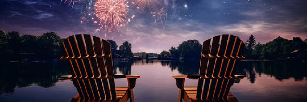Two Muskoka chairs on a deck with fireworks in the sky.