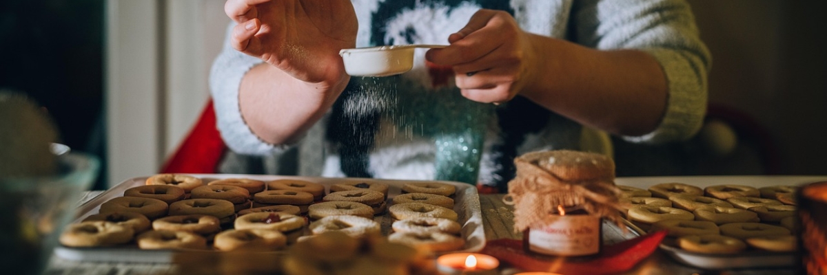 Woman sitting in front of a tray of baked goods. There are candles burning. She is sprinkling something on top.