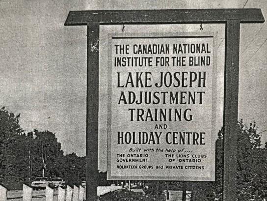 A black and white photo of the entrance sign to the Canadian National Institute for the Blind Lake Joseph Adjustment Training and Holiday Centre, 1965.