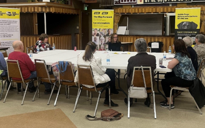Nine community members sit around a table having a conversation.