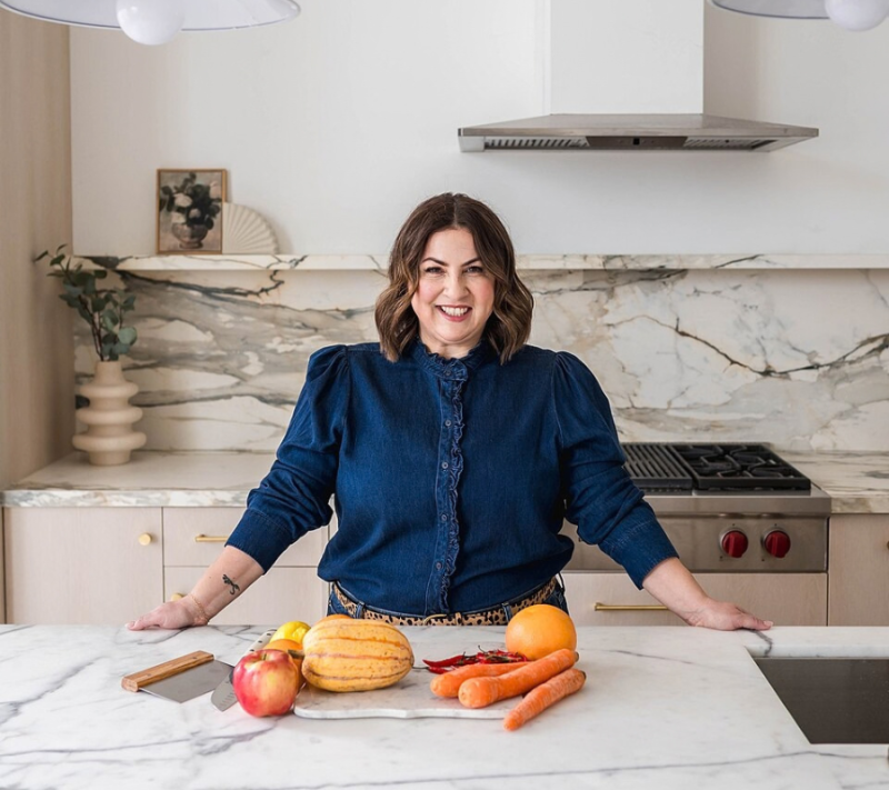 Mary Mammoliti standing in a kitchen studio with fresh ingredients on a marble countertop.