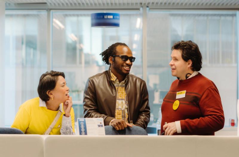 Three CNIB staff and volunteers smile and chat behind a table that has various brochures.