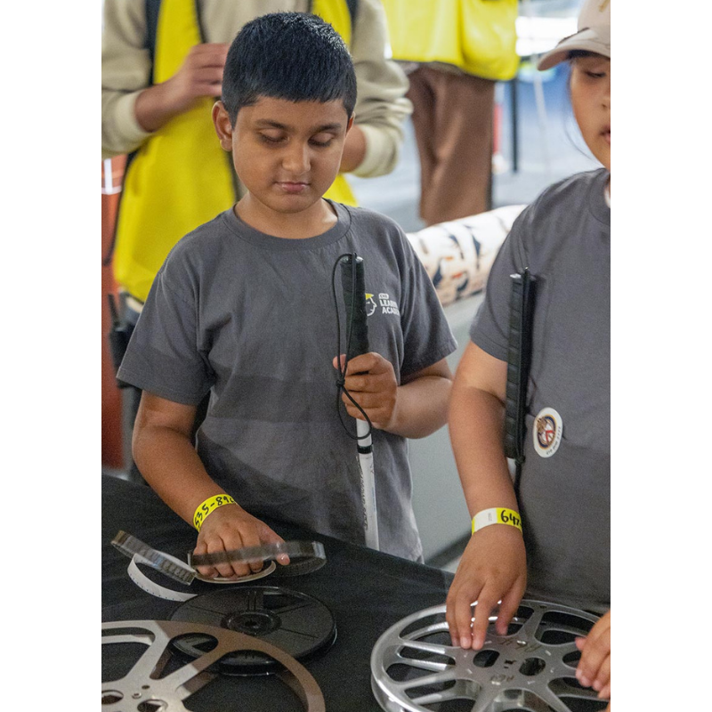 At the TIFF Lightbox, two young campers participate in a tactile touch tour, exploring the textures of various film reels with their hands.