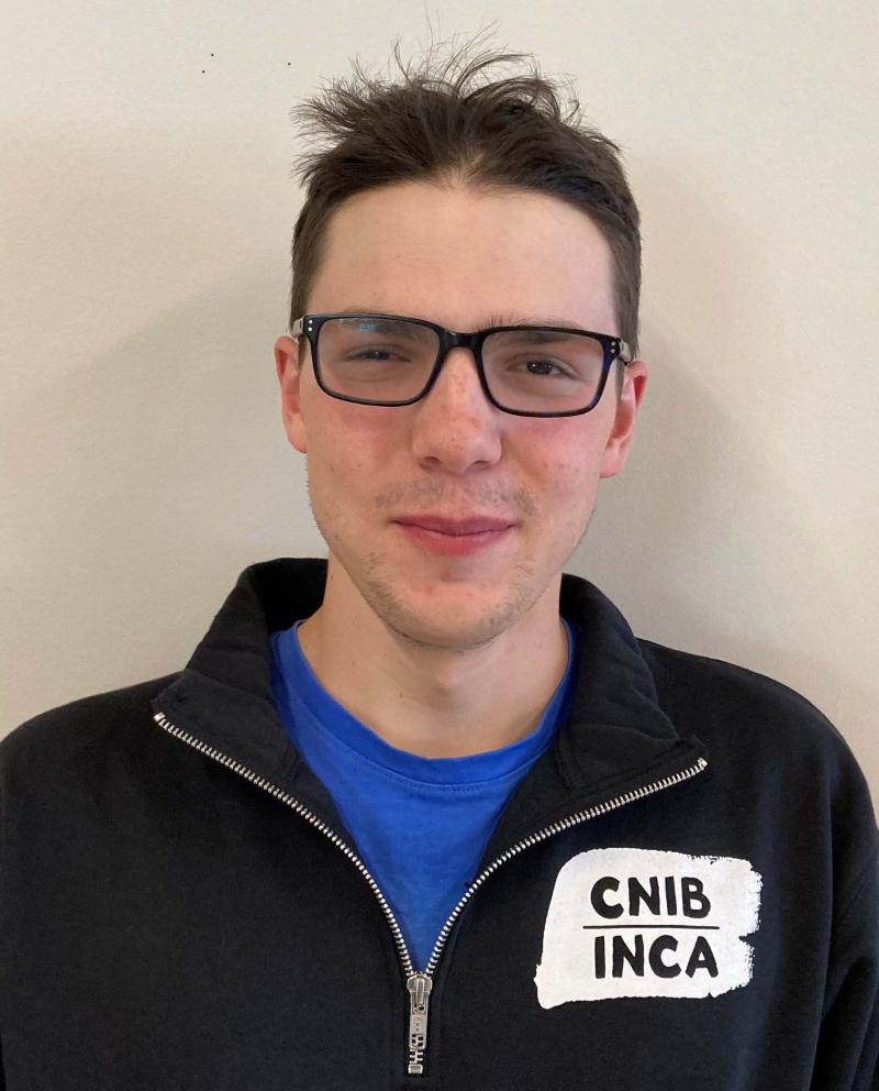 Curtis Ruttle wearing a CNIB/INCA sweater. Curtis wears glasses, has light skin and brown hair.