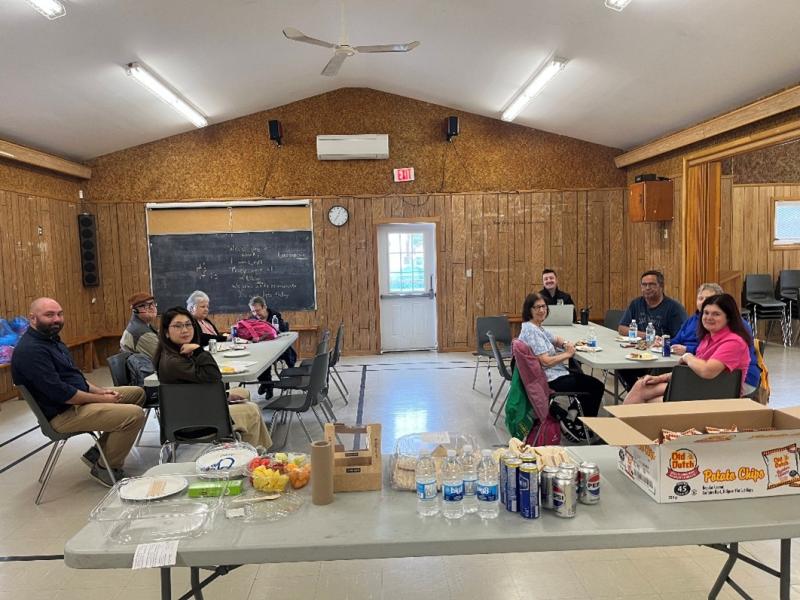 Participants gathered at an informational session about the Legal Support Program. Approximately 10 participants sit around two tables in a community meeting space, accompanied by a table with refreshments.