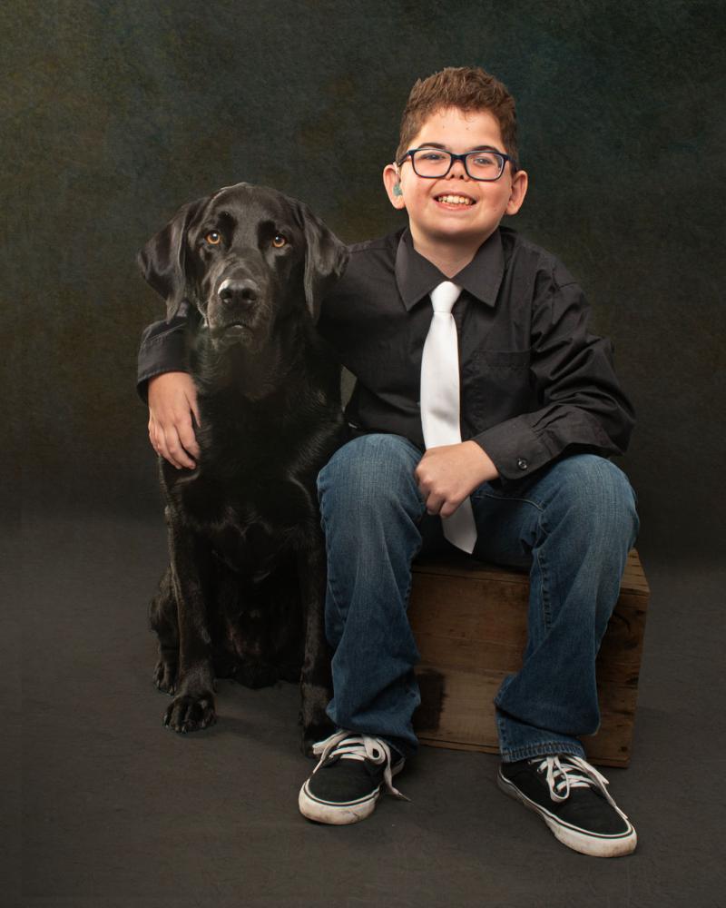 Kaiden and his buddy dog Flinn, a black Labrador Retriever, pose together for a photo.