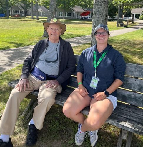 John sitting outdoors on a bench with a DBCS intervenor at CNIB Lake Joe, smiling together on a sunny afternoon.
