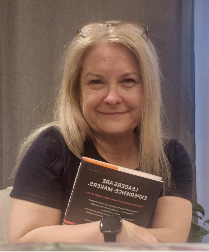 Mary Ellen is seated while hugging a hardcover book. She is smiling at the camera.