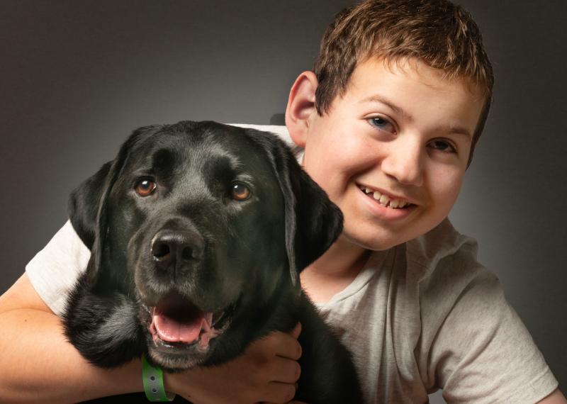 Ollie smiles and wraps his arms around his CNIB buddy dog, Hope.