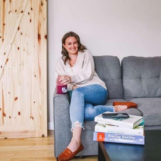 Skylar sitting comfortably on a couch holding a big glass of red juice.