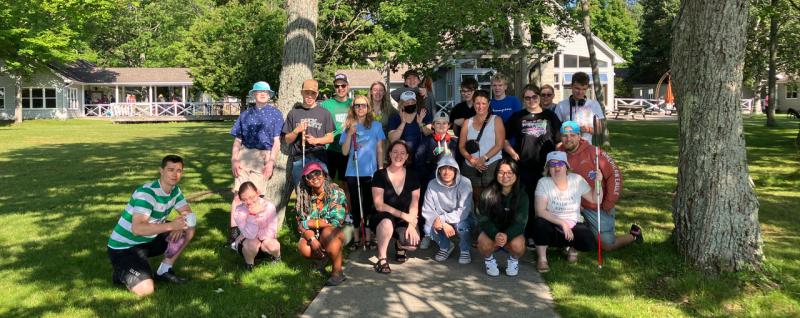 A large group of young adults, some of whom are holding white canes, pose together on a path at Lake Joe.