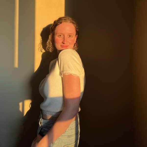 Taylor Gaudon posing looking over her left shoulder. The sunset is reflected on her and the wall behind her.