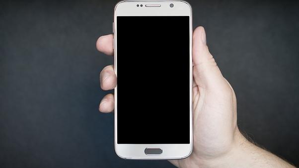 A hand holding an Android smartphone against a black background. 