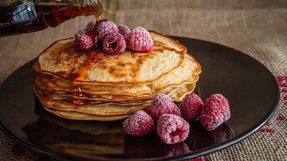 A stack of pancakes with maple syrup and raspberries. 