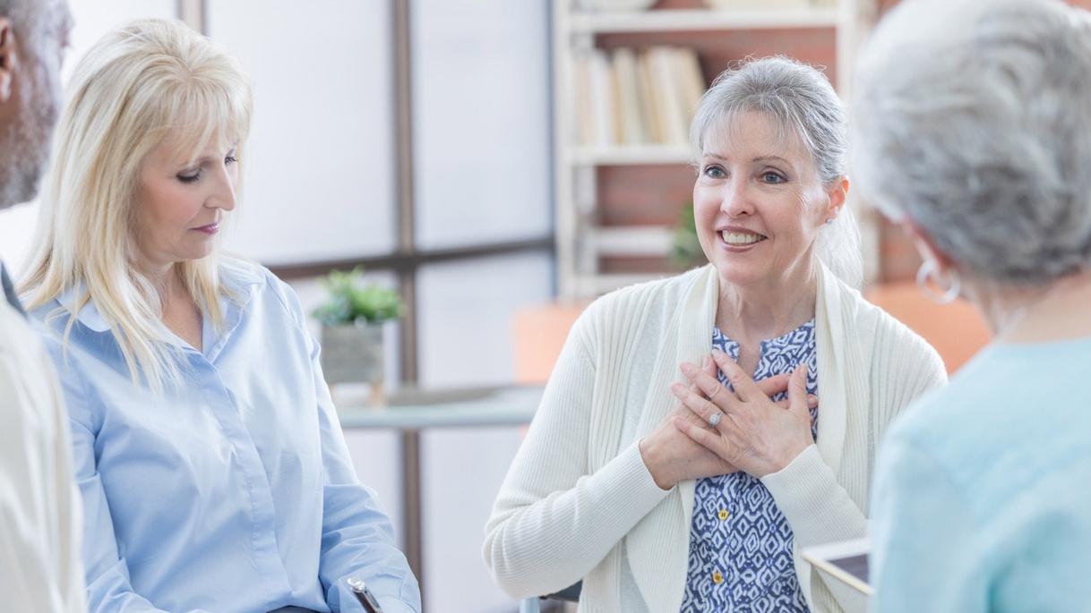 Three elderly women sit in a circle and engage in lively conversation. 