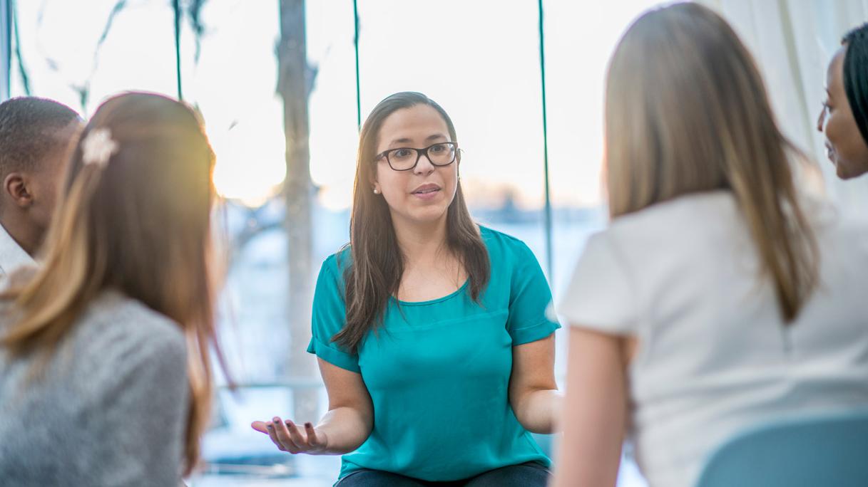 A group of five people sit in a circle and engage in lively conversation. 