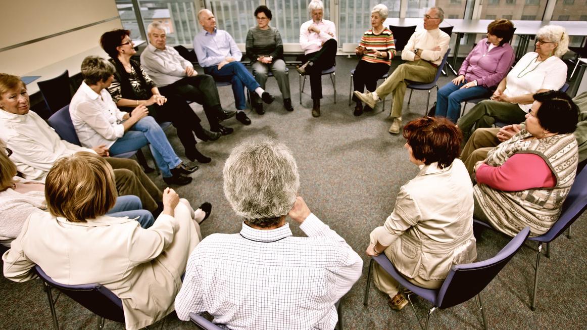 A group of 10 people sit in a circle and engage in lively conversation. 