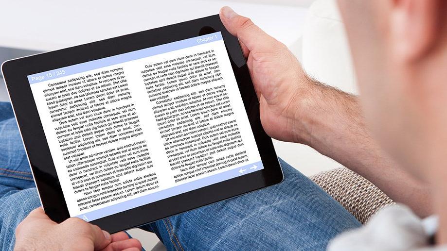 A person is sitting with their legs stretched out reading from an iPad