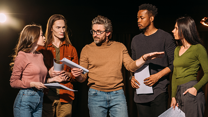 5 people in a group on a dark stage interacting with each other
