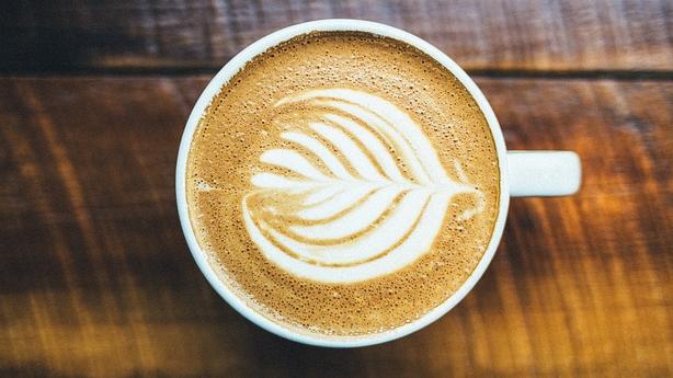 A cup sits on a table filled with an artisan cappuccino and foaming milk