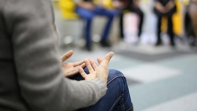 A person sits in a group circle. Their hands are clasped in their lap.