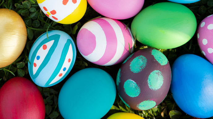A pile of colourful dyed easter eggs sit atop a grassy lawn. 