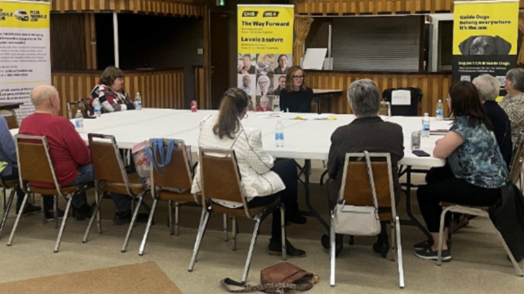 Nine community members sit around a table having a conversation. 