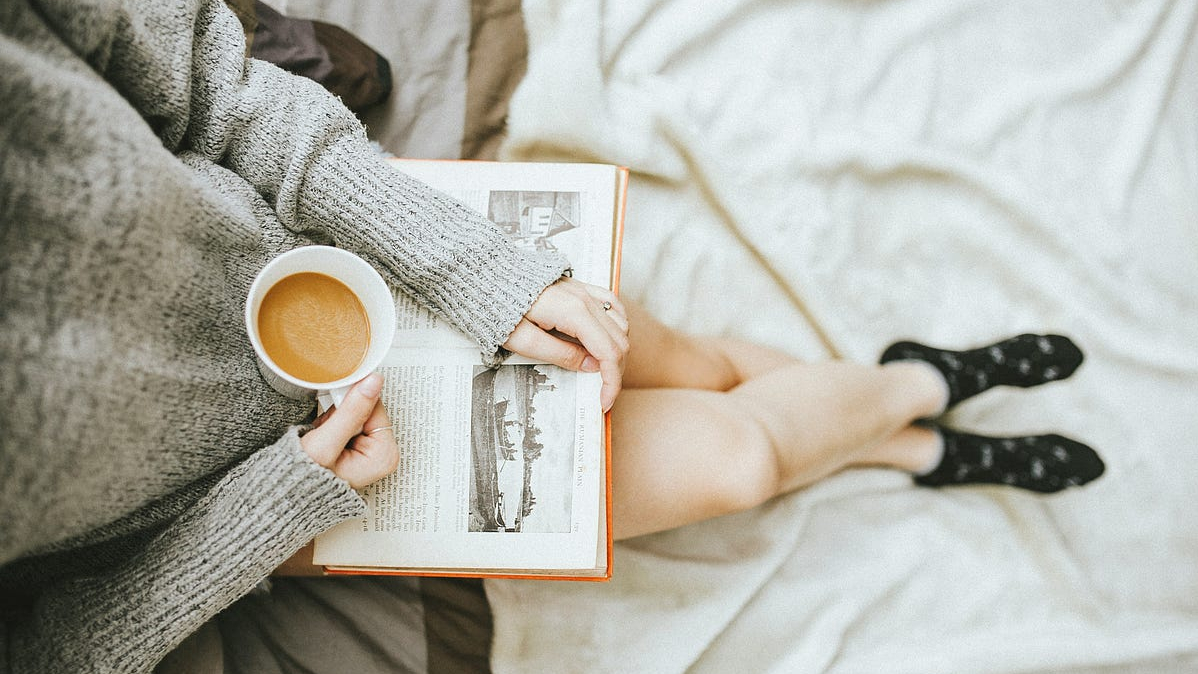 Birds eye view photo of a woman sitting with a coffee and a book on her lap.