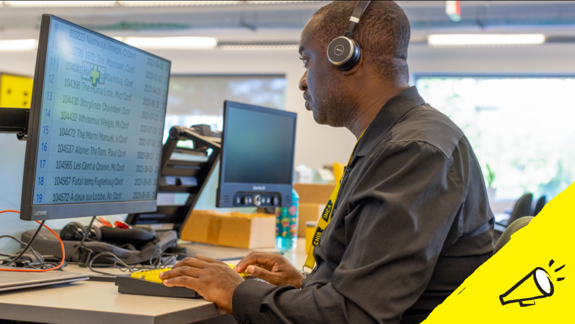 A man sits at a desk while using screen magnification technology on a desktop computer, as well as a high contrast keyboard