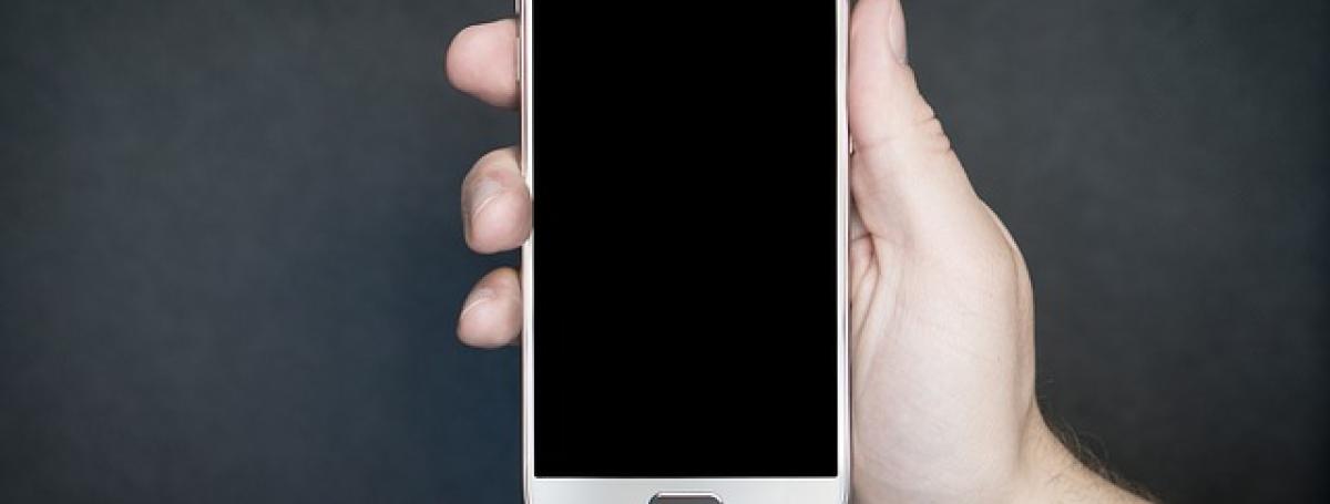 A hand holding an Android smartphone against a black background. 
