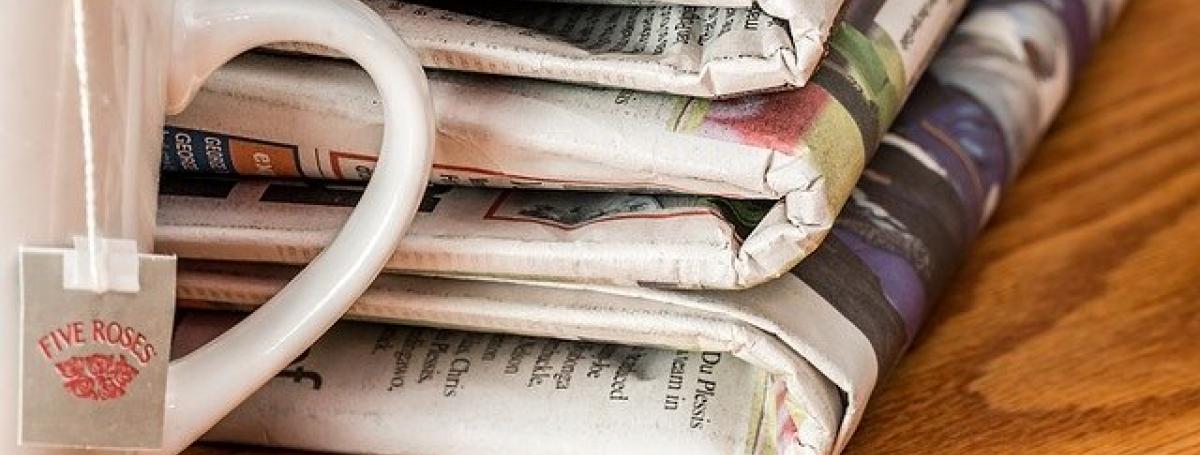 Three folded newspapers sits on a table next to a cup of tea. 