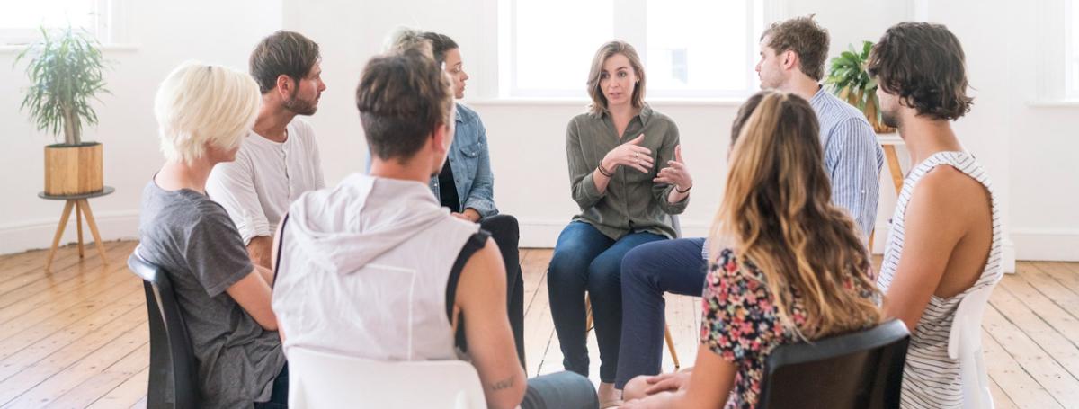 A support group of eight people sit in chairs in a circle and engage in lively conversation. 