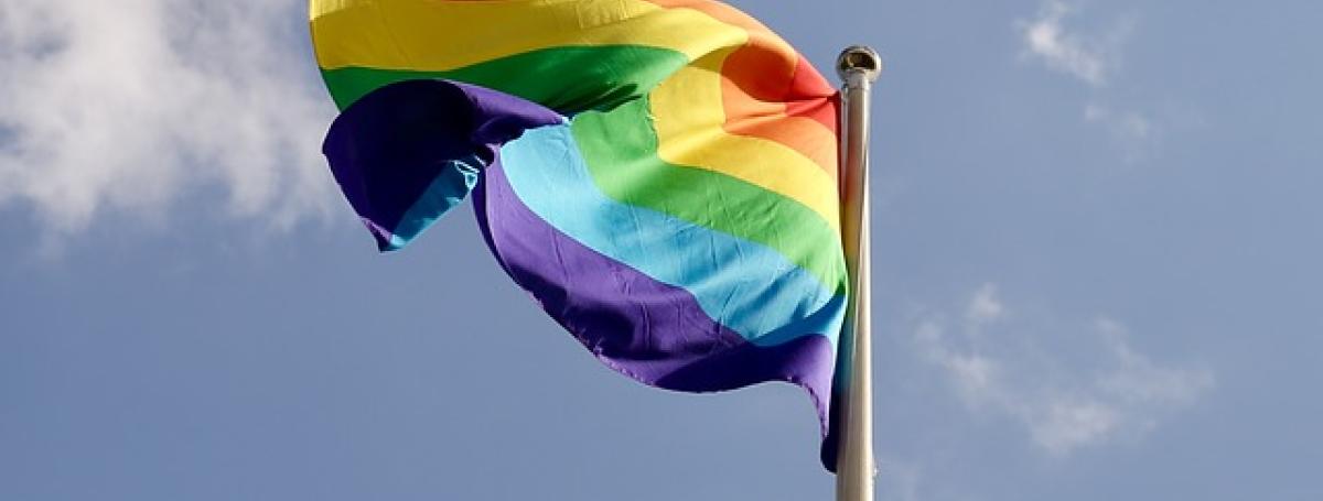 A colourful Pride flag waves in the wind on a flag post. 