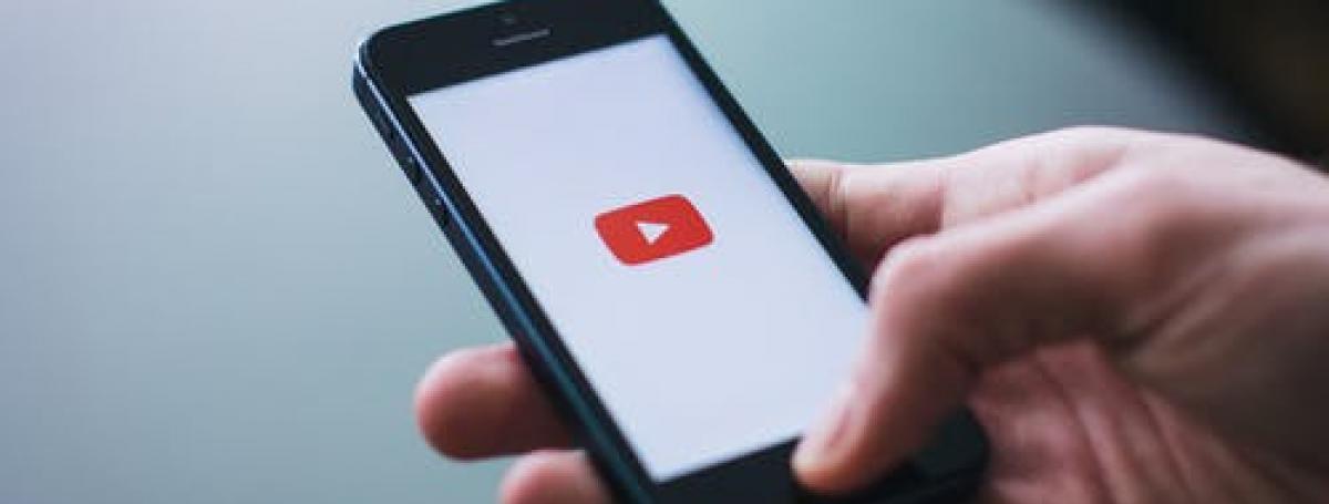 Une main tenant un smartphone avec le logo YouTube affiché sur l'écran.