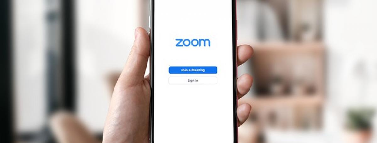 Une main tenant un iPhone. L'écran montre l'application Zoom.