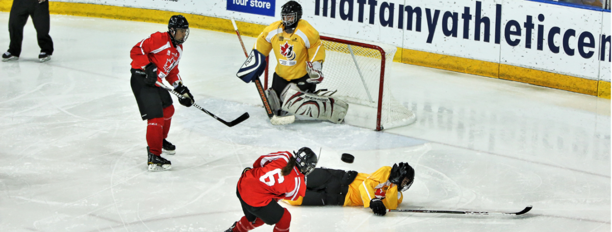 Canadian Blind Hockey tournament. A player shoots the puck at a goalie, and an opposing team member tries to block the goal.