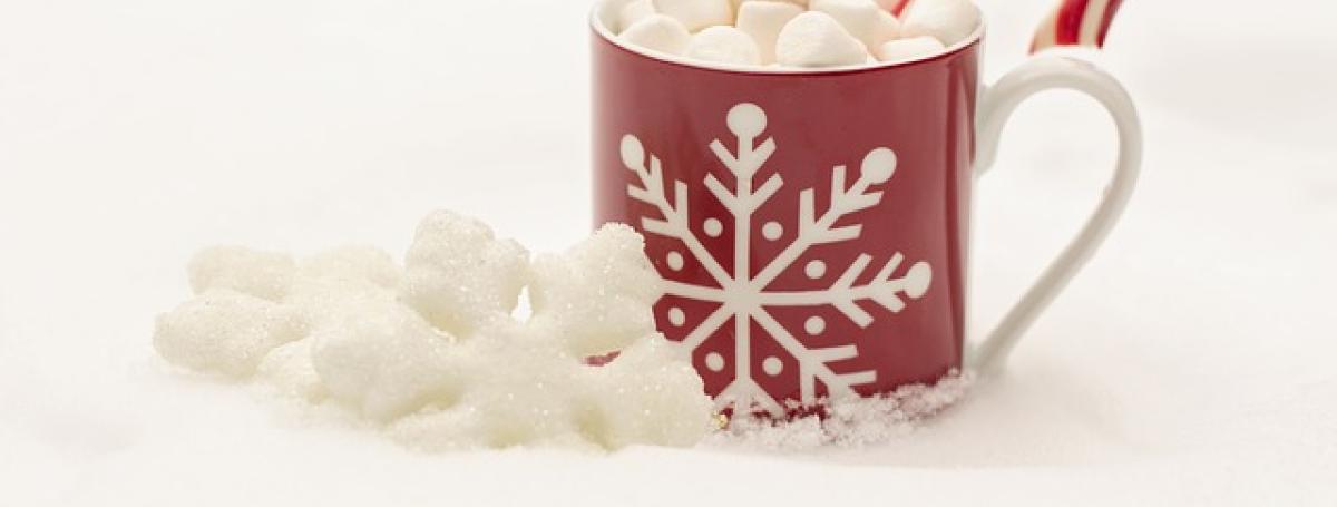 A cup of hot chocolate overflowing with marshmallows and a candy cane stick.