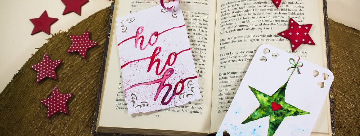 Open book with cards that say "ho ho ho" and one that has a green star shown with a heart in the middle. There are red stars floating.