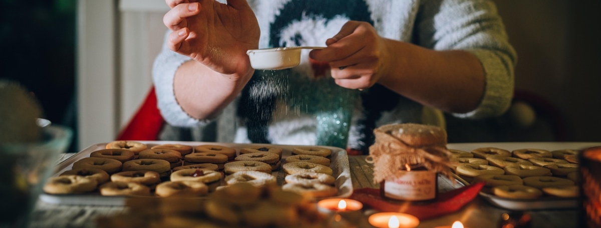 Woman sitting in front of a tray of baked goods. There are candles burning. She is sprinkling something on top.