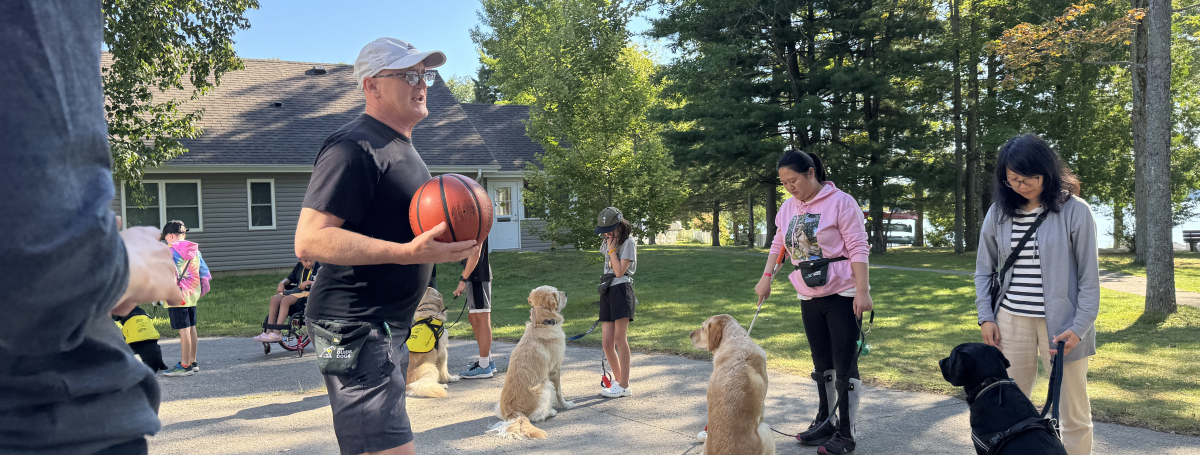 An instructor stands outside in front of a line of participants and guide dogs.
